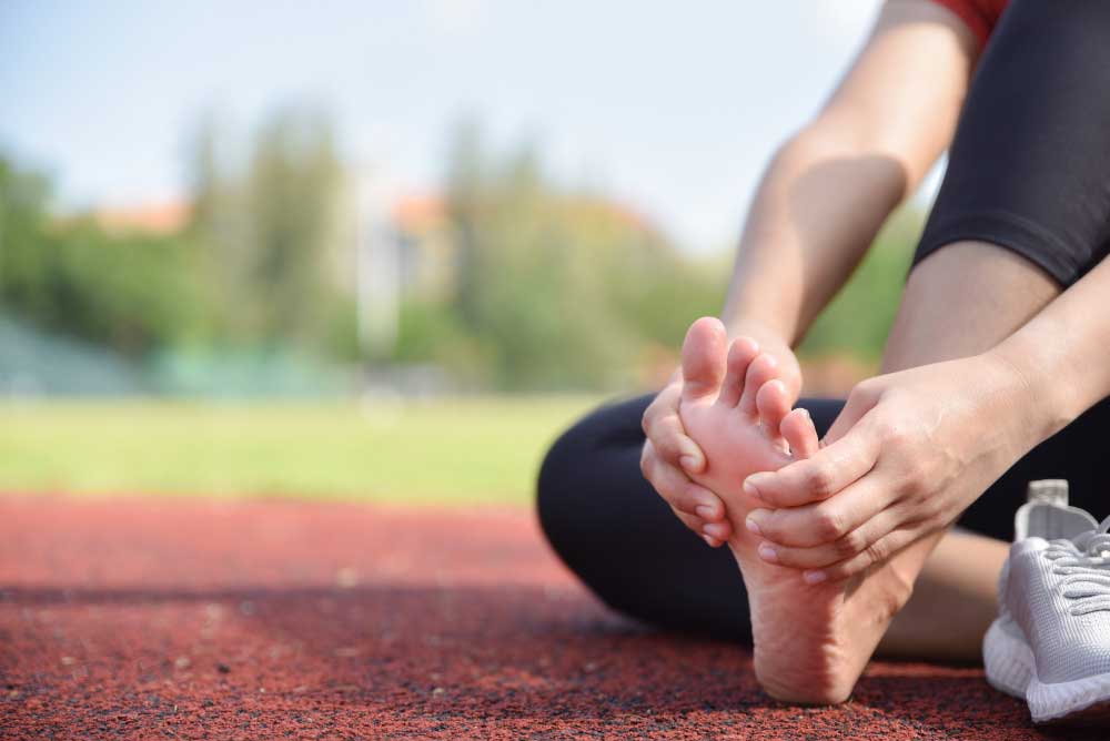 Athlete sitting on a running track holding their foot in pain after a workout, seeking treatment from a trusted Foot Doctor Cape Canaveral for foot injury and sports-related discomfort.