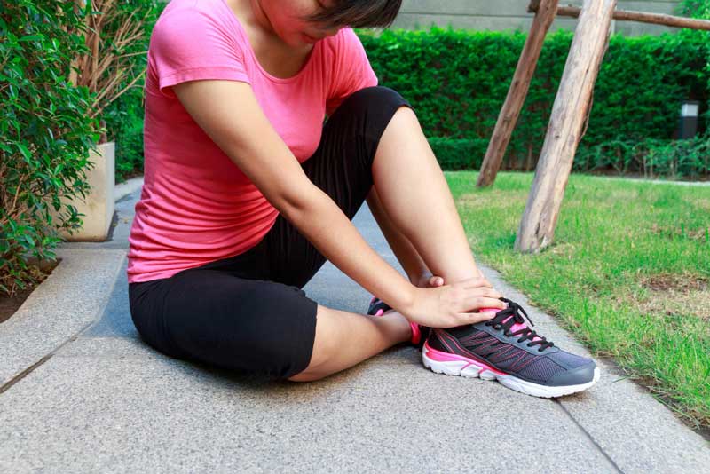 Woman sitting outdoors on a sidewalk holding her ankle in pain after exercise, highlighting the need for professional care from a trusted Foot Doctor Cape Canaveral for sports injury and foot pain relief.