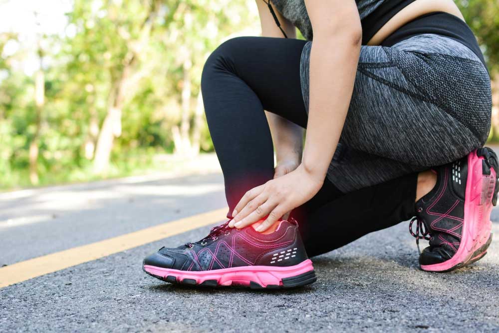 Athlete crouching on a running track holding her ankle in pain after jogging, emphasizing the need for expert treatment from a trusted Foot Doctor Cape Canaveral for ankle injuries and foot pain relief.