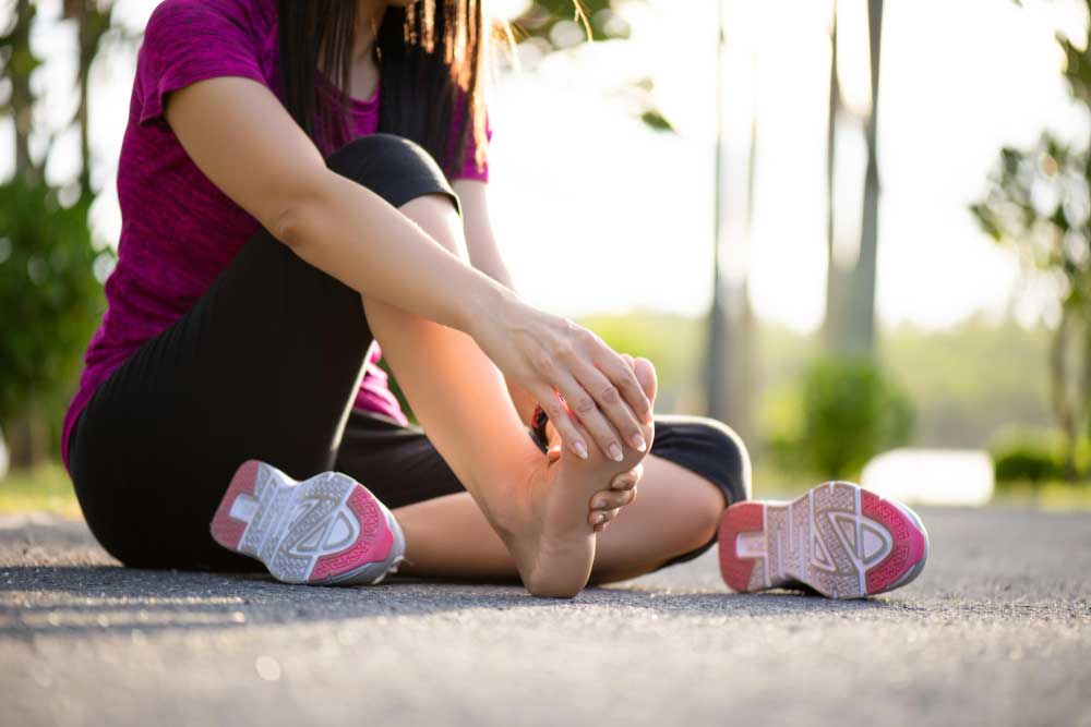 Woman sitting on a paved path holding her foot in pain after a workout, highlighting the importance of professional care from a trusted Foot Doctor Cape Canaveral for foot and heel pain treatment.