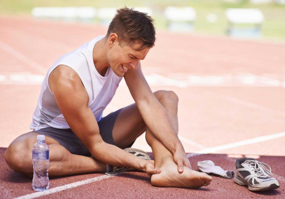 Athletic man sitting on a running track holding his injured foot in pain, emphasizing the need for expert care from a trusted Foot Doctor Rockledge for sports-related foot and ankle injuries.