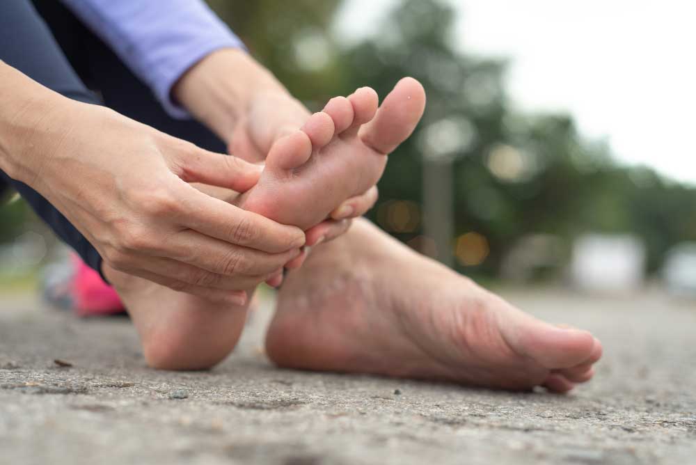 Person sitting outdoors holding the bottom of their foot in pain, highlighting heel and arch discomfort treated by an experienced Foot Doctor Rockledge for foot pain relief and podiatry care services.