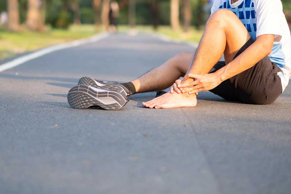 Athlete sitting on a road holding his ankle in pain after a run, illustrating sports injury and foot strain treated by a trusted Foot Doctor Rockledge for expert podiatry care and recovery.