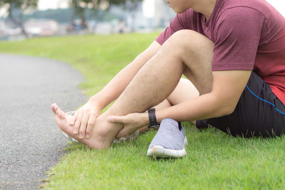 Man sitting on grass beside a running path holding his painful ankle after exercise, illustrating sports injury treatment and care from a trusted Foot Doctor Rockledge for foot and ankle pain relief.