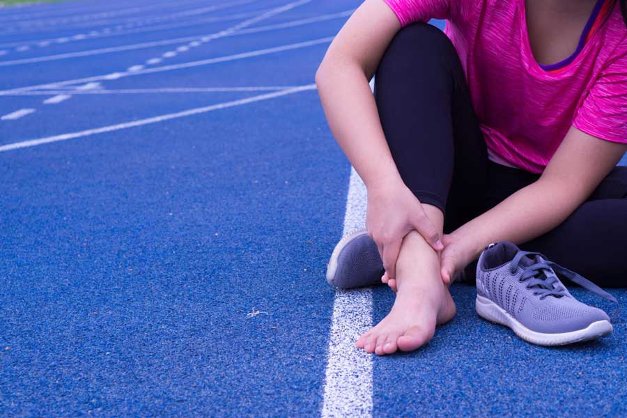 Athlete sitting on a running track holding her painful ankle after exercise, emphasizing sports injury treatment and expert care from a trusted Foot Doctor Rockledge for foot and ankle pain relief.