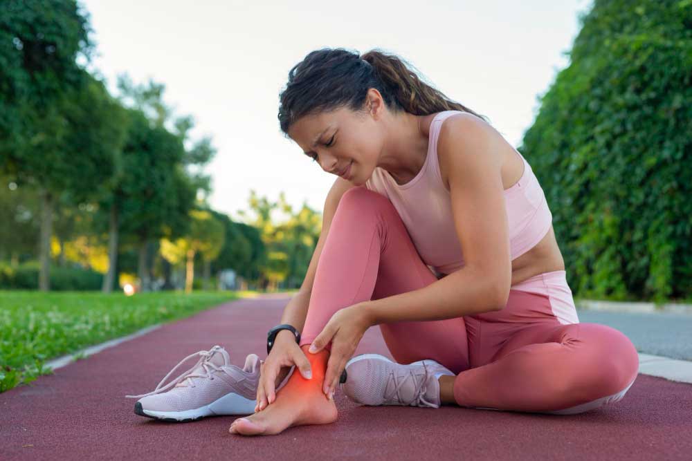 Athletic woman sitting on a running track holding her painful ankle with highlighted inflammation, seeking treatment from Foot Doctor Titusville for sports injury relief