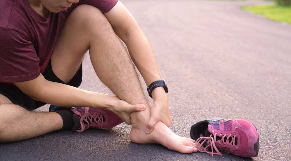 Male runner sitting on pavement holding his injured ankle after workout, highlighting need for expert care from Foot Doctor Titusville for sports-related foot pain and ankle injuries