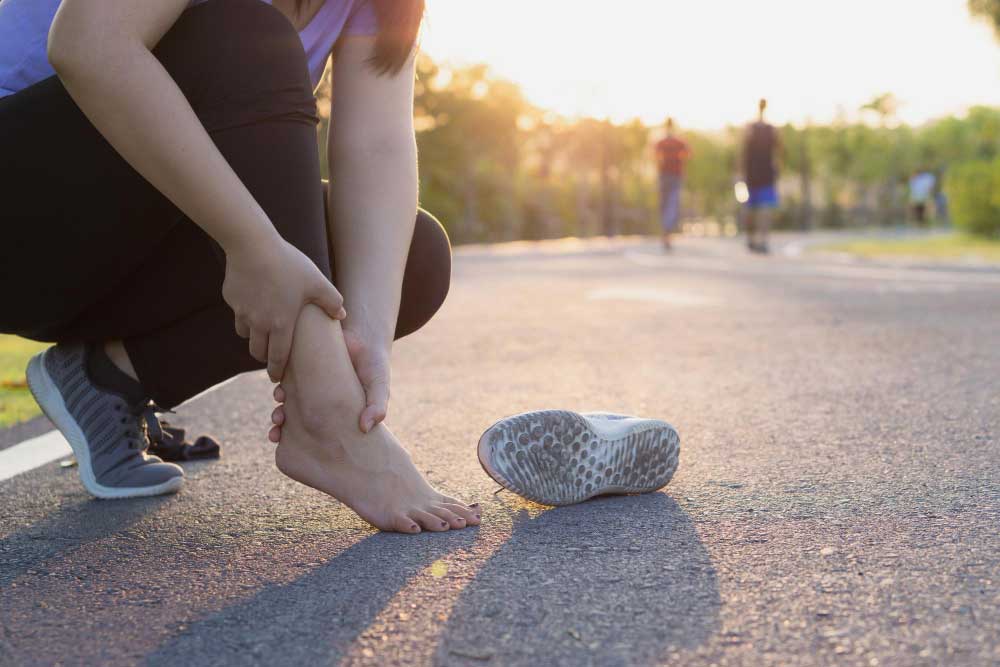 Woman crouching on a park pathway holding her sore ankle after a run at sunset, emphasizing need for professional treatment from Foot Doctor Titusville for ankle sprain and foot pain relief