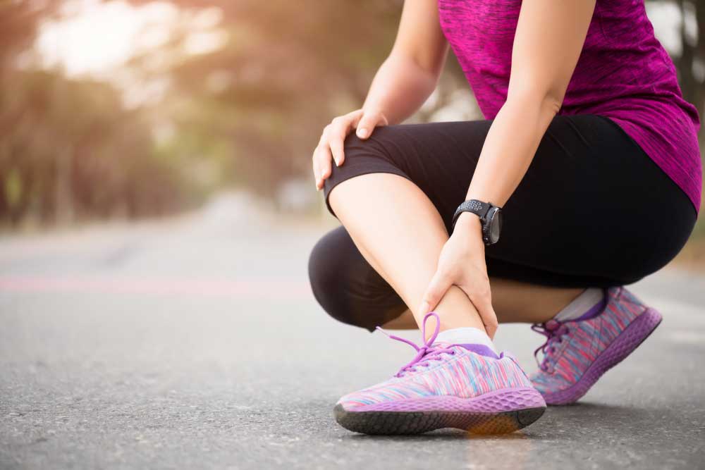Female runner crouching on the road holding her painful lower leg and ankle after workout, showing need for expert treatment from Foot Doctor Titusville for sports injury and foot pain relief