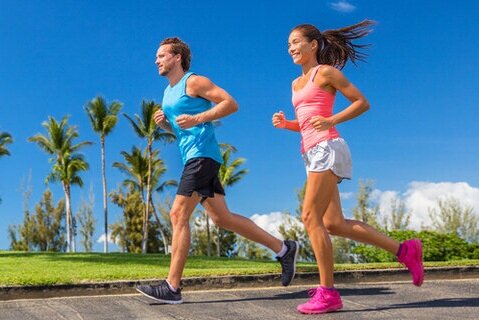 Man and woman jogging outdoors on a sunny day with palm trees in the background, representing active lifestyle and sports injury prevention supported by expert care from merritt island foot and ankle.